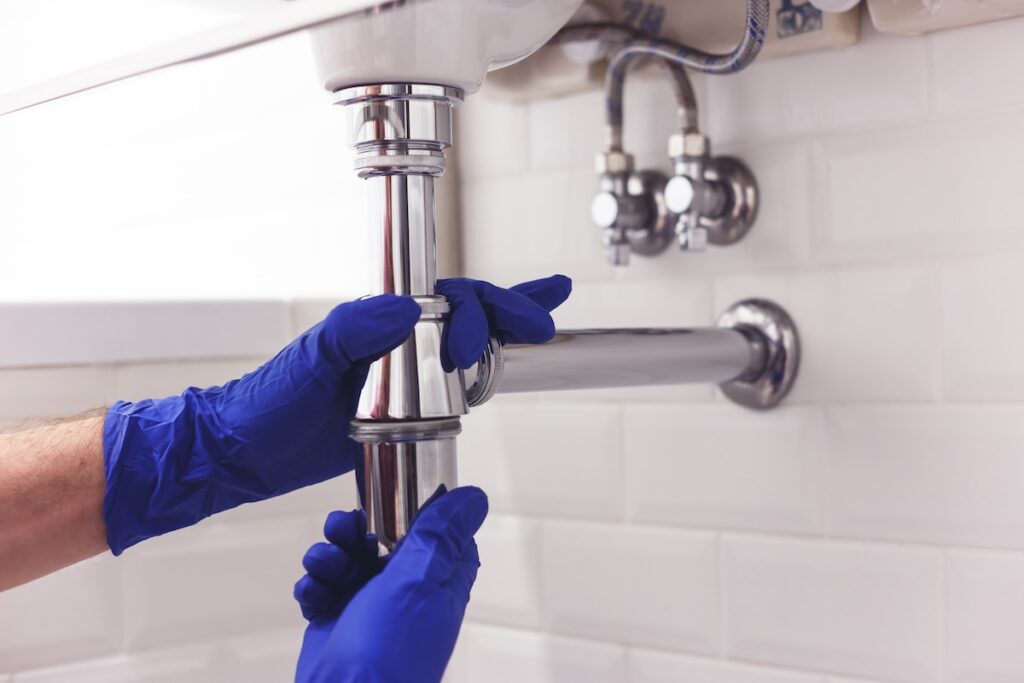 Plumber repairs and maintains chrome siphon under the washbasin. Plumber at work in bathroom, plumbing assemble and install concept. SSUCv3H4sIAAAAAAAACpyRz27DIAzG75P2DhHnRmqhSZq+SrWDA26CSqECsmmq+u7jT6g474Z/tj/7M8/Pj6YhEzjJybl5xijEUqnVeQteGh3wfrdxi1qgrQkK6Y2VoGo4geeLhjsGqFelIn6lJHEe/OrQxWEb4uBxDhoZviXyRpccNyWRkqEjpAjZVcytU2IFZfF/debHV3EDM2r+mxaujFhUCNnIJZeS249He6+twSqkqVx9Gw4qFrBK6WEll3qu2oxf0pVLGzer9jau8N6cKGMeMKl44mvQxMIXcC6Ui8KrQTz8qblXc7TxycCmSkT4iRgeGKV0YKynw9B3J8boVpB/b5FBJ61ThELMb1LU1mXcgPBuxP3IaSsQx/bIB9qOp+uhpXAUDFnHOtGHw7/+AAAA//8DAGfsxPyHAgAA